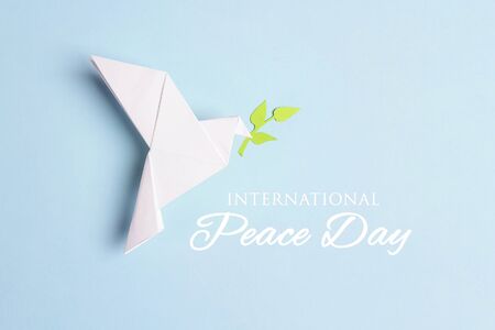 World Peace Day greeting card. Paper origami dove of peace with olive branch and text on a blue background.の写真素材
