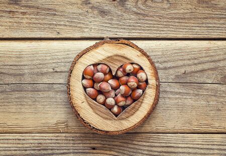 Hazelnut in a carved wooden heart on old wooden background. Space for text. Top view.