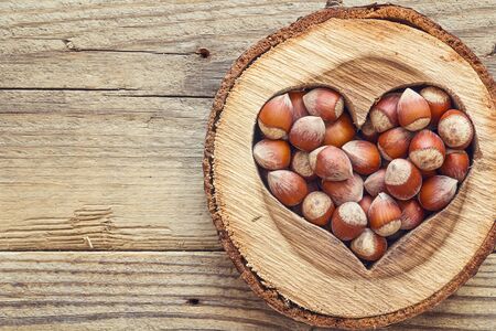 Hazelnut in a carved wooden heart on old wooden background. Space for text. Top view.