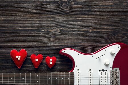 Red electric guitar with hearts on a dark wooden background. Valentine's Day background. Space for text. Top view.の写真素材