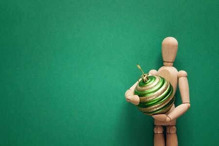 Classic wooden dummy holds Christmas ball on a green background. Space for text.の写真素材