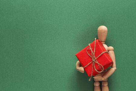 Classic wooden dummy holds Christmas gift on green background. Space for text.の写真素材