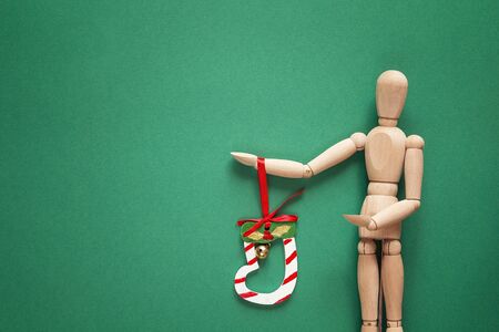 Classic wooden dummy holds Christmas bell on a green background. Space for text.