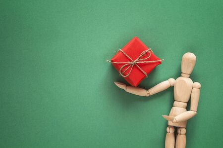 Classic wooden dummy holds Christmas gift on green background. Space for text.の写真素材