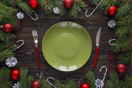 Empty green plate with knife and fork and Christmas decorations on wooden table. Christmas table setting. View from above.の写真素材