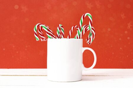 White coffee mug with Christmas candy canes on red background. Space for text or design.の写真素材