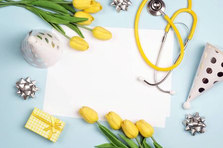 Doctor's or nurse day greeting card with stethoscope, yellow tulips and festive caps on blue background. Copy space for text.の写真素材