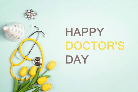 Doctor's day greeting card with stethoscope, yellow tulips and festive caps on blue background.の写真素材