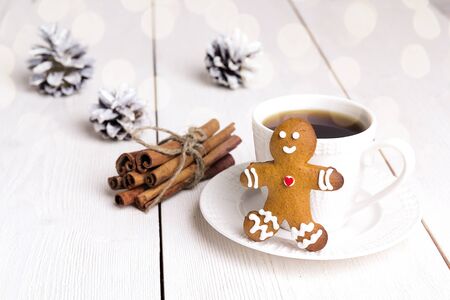 Cup of coffee  with gingerbread man and cinnamon sticks on white wooden table. Traditional beverage...
