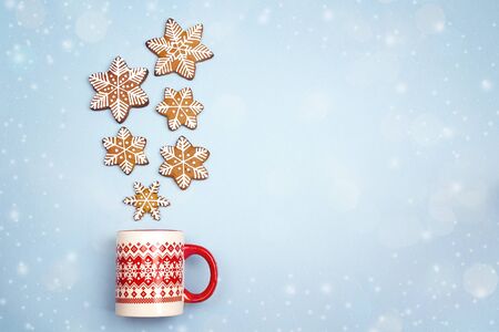 Snowfall from gingerbread snowflakes in Christmas mug on blue background. Copy space. Christmas...