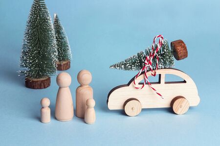 Toy family and toy car with Christmas tree on the roof. Wooden figures of father, mother and children who went by car to the forest for the Christmas tree. Symbolic concept of winter family holidays.の写真素材