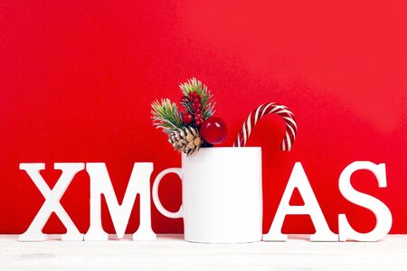White coffee mug with word Xmas, candy cane and decorative branch on red background. Space for text...