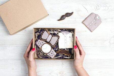 Box of gingerbread cookies in female hands on light wooden table. Creative male style gingerbread  in the shape of a shirt, watch, bow tie and mustache. International men's day or Father's Day concept.の写真素材