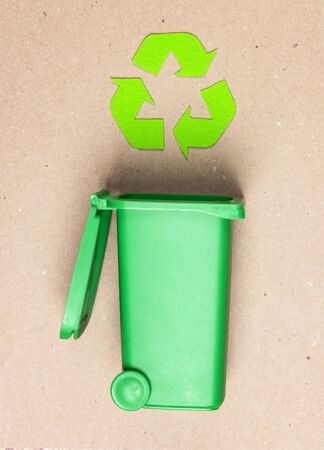 Green trash bin with recycling symbol on brown paper background.の写真素材