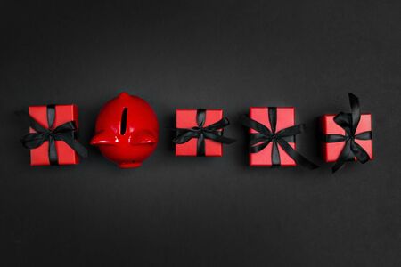 Red gift boxes with black ribbons and piggy bank on a black background. Holiday or black friday concept. Top view with copy space.の写真素材
