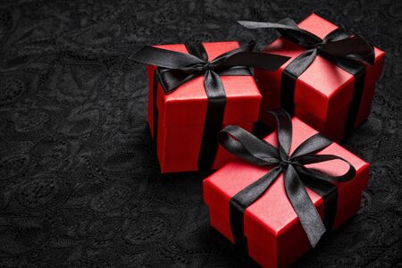 Red gift boxes with black ribbons on a black lace background. Holiday or black friday concept.の写真素材