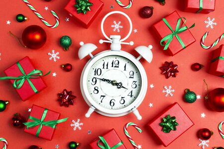 Christmas alarm clock with gift boxes and decorations on a red background. Christmas timer. Time to...