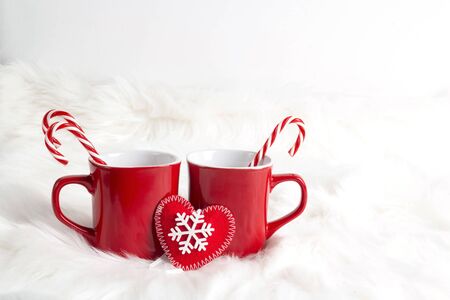 Two red mugs with candy cane on white fur background. Hot drinks: cocoa, chocolate, coffee or tea.の写真素材