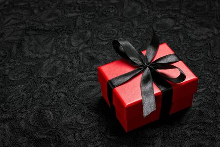 Red gift box with black ribbon on a black lace background. Holiday or black friday concept.の写真素材