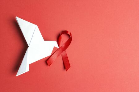 Origami paper dove with red ribbon as symbol of aids awareness on red background.1 december World...