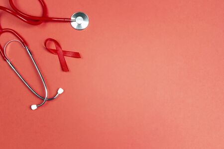 Red ribbon as symbol of aids awareness with stethoscope on red background. 1 december World Aids Day...