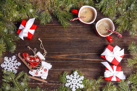 Festive background with two coffee mugs, fir branches, toy skates and gifts on wooden table. Space for text, top view.の写真素材