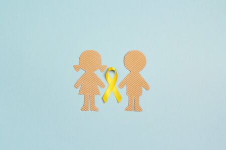Childhood Cancer Awareness Yellow Ribbon with boy and girl cardboard dolls on blue background. Childhood Cancer Day February, 15.の写真素材