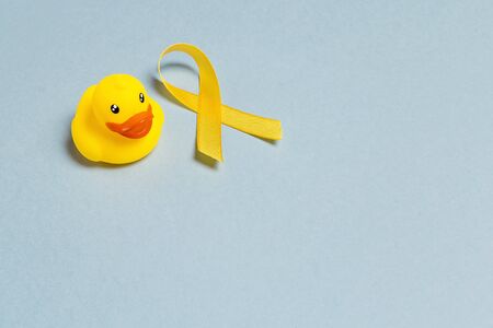 Children's toy and a Childhood Cancer Awareness Yellow Ribbon on blue background with copy space. Childhood Cancer Day February, 15.の写真素材