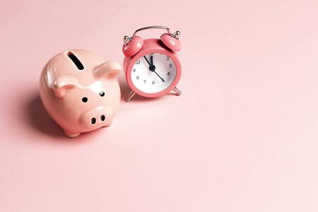 Piggy bank and classic alarm clock on pink background. Time to saving, money, banking concept.  Flat design, copy space for text.の写真素材