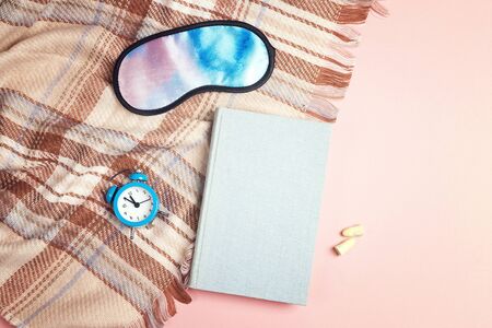 Book, sleeping mask, alarm clock, earplugs and plaid on pink background. Healthy sleep concept. Top down composition on with copy space.の写真素材