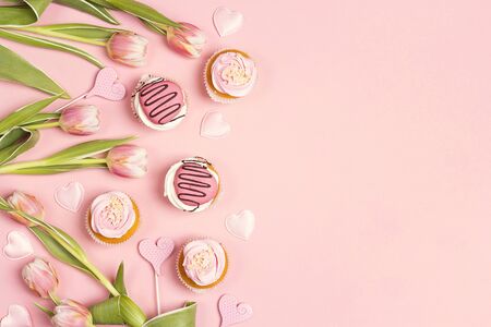 Border of tasty cupcakes with tulips on pink pastel background. Romantic love background. St. Valentine, Mothers, Womens Day concept. Copy space, overhead shot. の写真素材