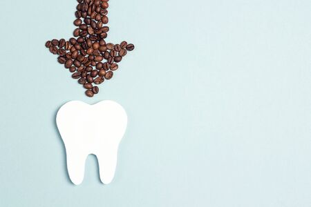 Tooth and coffee bean arrow on a blue background. Coffee spoils teeth and makes them yellow. Oral...