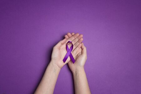 Hands holding Purple ribbons on a purple background. World epilepsy day. Alzheimer's disease, Pancreatic cancer, Epilepsy awareness, fibromyalgia awareness.の写真素材