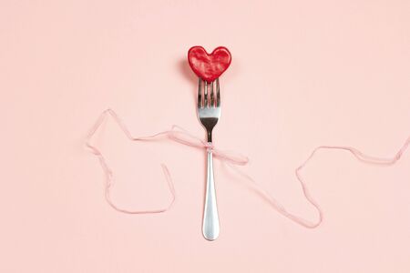 Fork with a heart and ribbon on pink table. Festive menu for Valentine's Day. Top view.