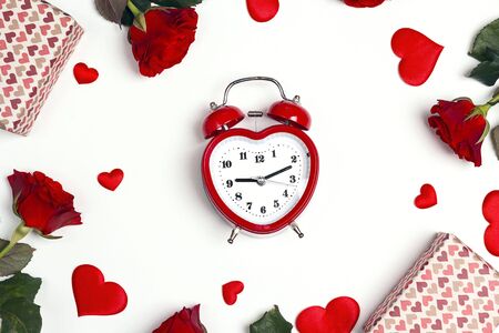 Romantic alarm clock with gifts, rose flowers and decorative hearts on white background. Top down composition. St. Valentines Day concept. 
の写真素材