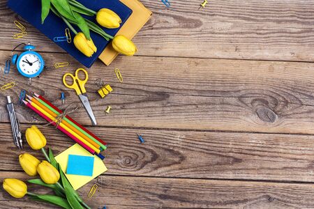 Festive educational background with school supplies and tulip flowers on rustic wooden table. Copy space for text. The concept of the teacher's day. Card, invitation or greeting template.の写真素材