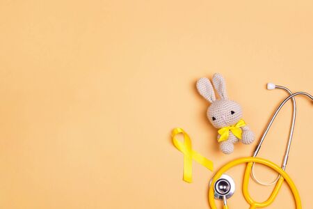 Childhood Cancer Awareness Golden Ribbon with toy bunny and stethoscope on yellow background with copy space. Childhood Cancer Day February, 15.の写真素材