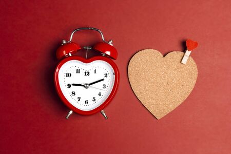 Romantic alarm clock and cork heart with clothespin on red background. Place for text. Top view, flat lay.の写真素材