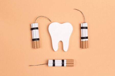 Tooth with cigarettes dynamite on yellow background. Smoking effect on human teeth. Dental care...
