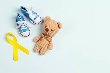 Childhood Cancer Awareness Yellow Ribbon with toy bear and baby sneakers on blue background. Childhood Cancer Day February, 15.の写真素材