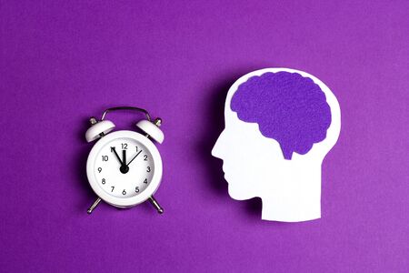 Head silhouette with a purple brain and white alarm clock on a purple background. Epilepsy disease or Alzheimer disease awareness world day.の写真素材