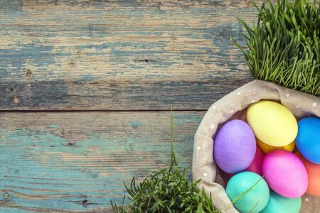 Basket with Easter eggs and green grass on old painted boards. Space for text. Top view.