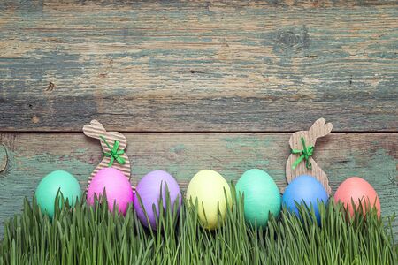 Easter eggs in fresh green grass on old wooden background. Space for text.