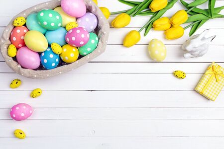 Basket with Easter eggs and yellow tulips on a white wooden table. Space for text. Top view.の写真素材