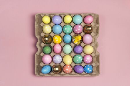 Many colored Easter eggs on tray on a pink background. Top view.