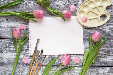 Art album, paintbrushes, palette and pink tulips on gray wooden background. Copy space. Top view.の写真素材