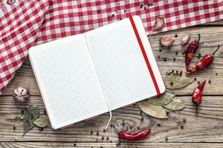 Blank open cookbook with condiments and a checkered napkin on an old wooden table. Copy space, top view.の写真素材