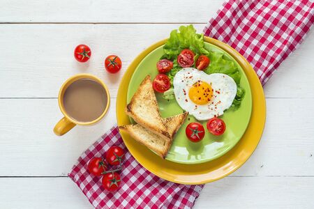 Healthy Breakfast with heart-shaped fried egg, toast, cherry tomato, lettuce on colored plates and coffee. Top view.
の写真素材