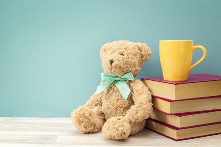 Plush bear with stack of book and yellow mug against blue background. Copy space for text. Education background.の写真素材