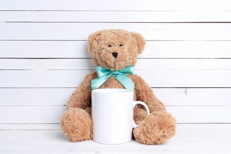 White coffee mug with plush bear on white wooden background. Space for text or design.の写真素材